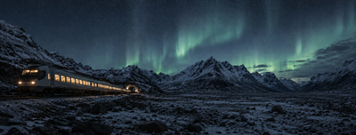Passenger train approaching a tunnel portal in a snow-covered mountain valley under the northern lights