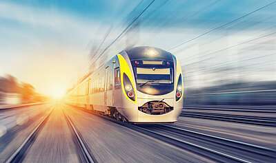 Modern passenger train travelling at speed on open track at sunrise